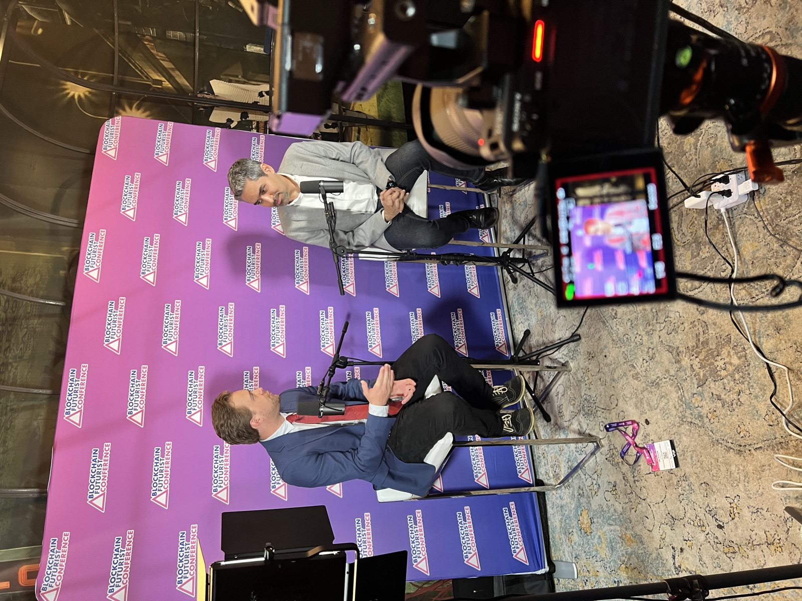 Agnic being interviewed on camera in front of a Blockchain Futurist Conference step-and-repeat backdrop